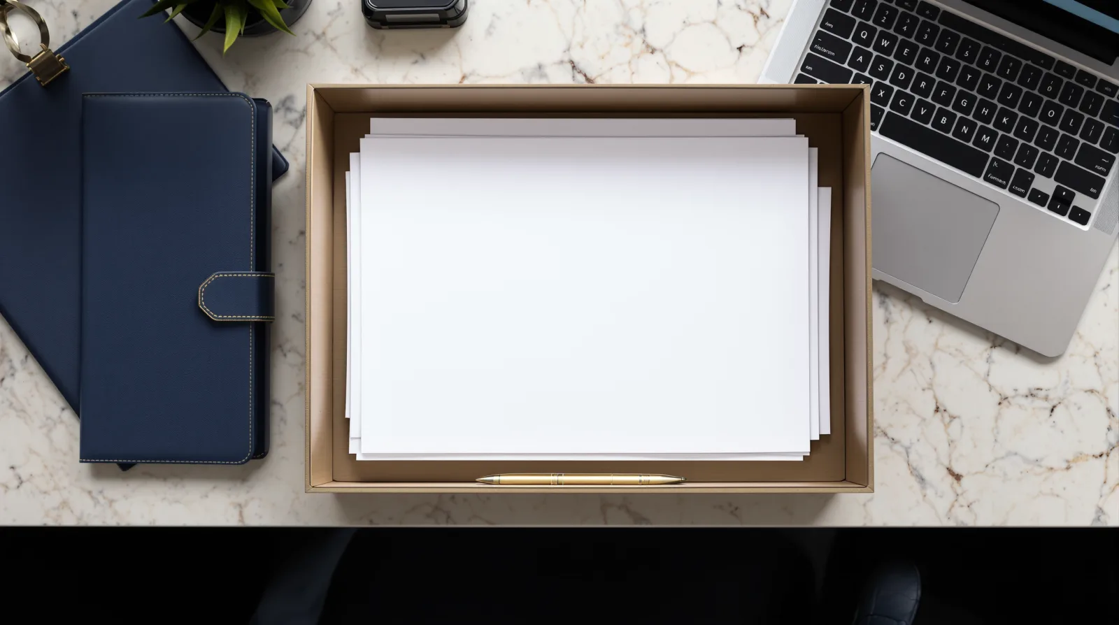 Top-down view of a tidy desk with a paper intake tray, a laptop, and a navy folder